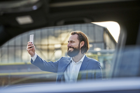 Lächelnder Geschäftsmann macht ein Selfie vor dem Auto, lizenzfreies Stockfoto