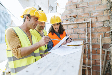 Woman and two construction workers talking on construction site - KIJF01240