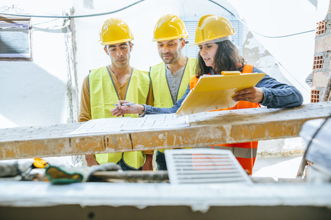 Frau im Gespräch mit zwei Bauarbeitern auf einer Baustelle, lizenzfreies Stockfoto