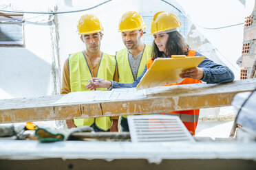 Woman talking to two construction workers on construction site - KIJF01241