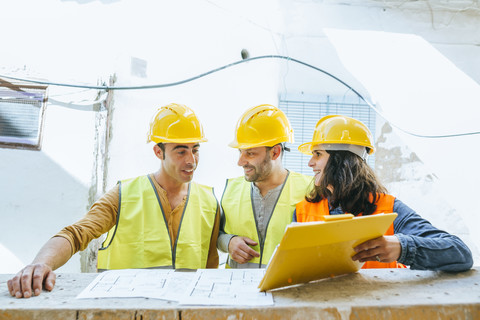 Woman showing clipboard to two construction workers on construction site stock photo