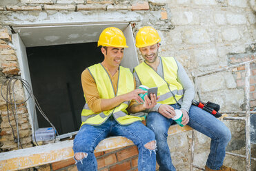 Zwei Bauarbeiter schauen in der Pause auf ein Handy - KIJF01247