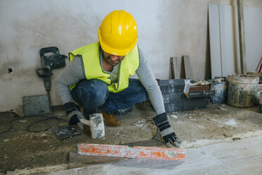 Bauarbeiter verlegt Bodenbelag mit einem Hammer - KIJF01256