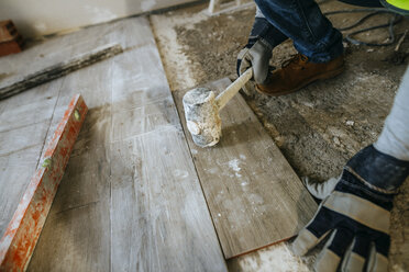 Nahaufnahme eines Bauarbeiters, der einen Bodenbelag mit einem Hammer verlegt - KIJF01258