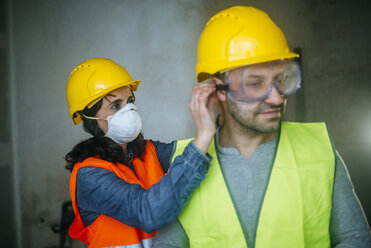 Frau hilft Mann beim Aufsetzen der Schutzbrille auf einer Baustelle - KIJF01263