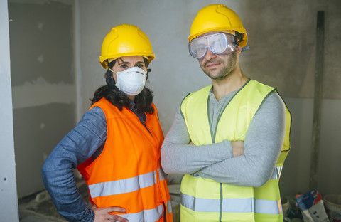 Porträt einer Frau mit Maske und eines Mannes mit Schutzbrille auf einer Baustelle, lizenzfreies Stockfoto