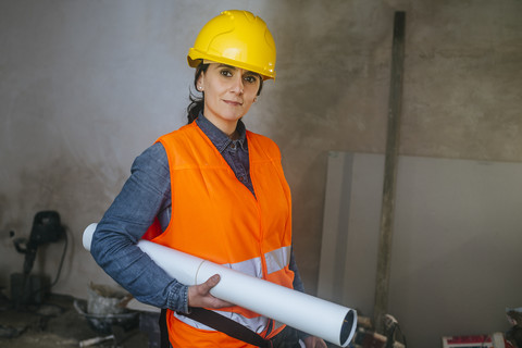 Frau mit Schutzhelm und reflektierender Weste auf Baustelle mit Blaupause,  lizenzfreies Stockfoto