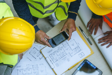 Woman and two men in workwear taking cell phone picture of a construction plan - KIJF01271