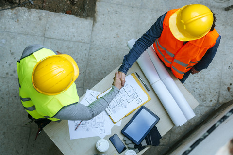 Woman and man in workwear shaking hands above construction plan stock photo