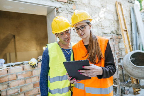 Frau mit Tablet im Gespräch mit Bauarbeiter auf einer Baustelle - KIJF01277