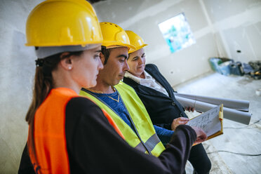 Zwei Frauen und ein Bauarbeiter auf einer Baustelle betrachten einen Plan - KIJF01280