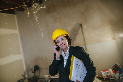 Woman wearing hard hat talking on phone on construction site stock photo