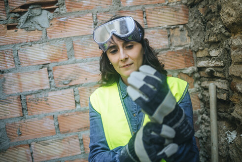 Frau auf einer Baustelle zieht Schutzhandschuhe an - KIJF01290