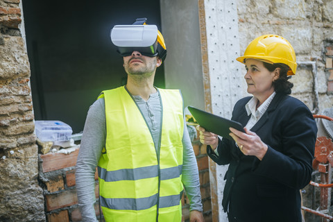 Frau mit Tablet und Bauarbeiter mit VR-Brille auf einer Baustelle, lizenzfreies Stockfoto