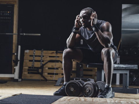 Sportler, der im Fitnessstudio sitzt, Kopfhörer trägt und sich konzentriert, lizenzfreies Stockfoto