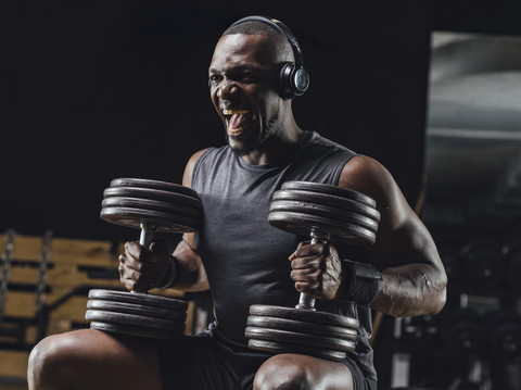 Sportler beim Training mit Hanteln im Fitnessstudio, schreiend, lizenzfreies Stockfoto