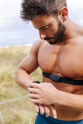 Barechested athlete outdoors looking on smartwatch - MGOF03007
