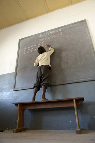 Madagaskar, Fianarantsoa, Schuljunge schreibt an Tafel, lizenzfreies Stockfoto