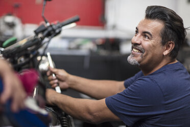 Smiling mechanic working on motorcycle in workshop - ZEF13017