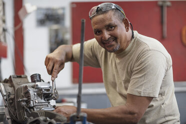 Lächelnder Mechaniker bei der Arbeit an einem Motorradmotor in einer Werkstatt - ZEF13020