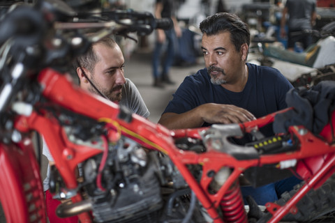 Zwei Mechaniker arbeiten gemeinsam an einem Motorrad in einer Werkstatt, lizenzfreies Stockfoto