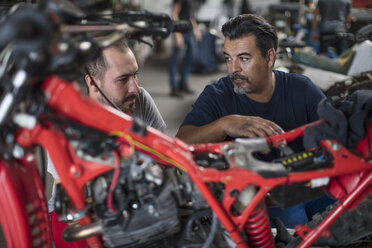 Zwei Mechaniker arbeiten gemeinsam an einem Motorrad in einer Werkstatt - ZEF13024