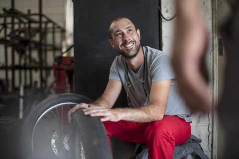 Lächelnder Mechaniker in der Werkstatt, der einen Kollegen ansieht, lizenzfreies Stockfoto