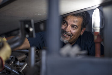 Lächelnder Mechaniker bei der Arbeit an einem Motorrad in einer Werkstatt - ZEF13048