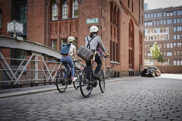 Germany, Hamburg, back view of couple riding electric bicycles at Old Warehouse District - RORF00640