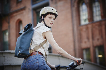 Porträt einer jungen Frau mit Fahrradhelm und Rucksack auf einem Elektrofahrrad - RORF00642