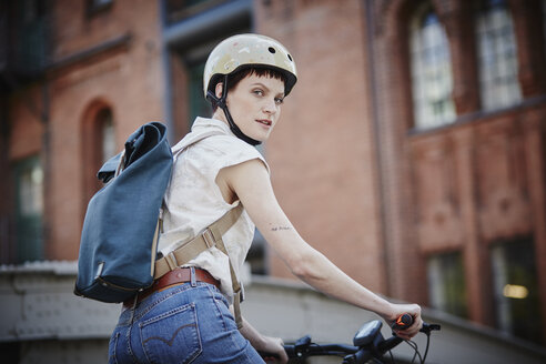 Portrait of young woman with cycling helmet and backpack on electric bicycle - RORF00642