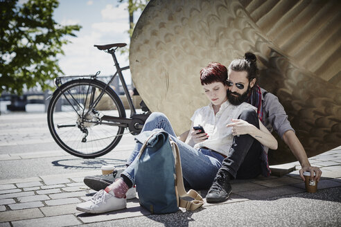 Germany, Hamburg, couple on bicycle trip having a rest looking at cell phone - RORF00644