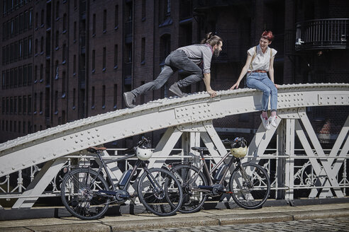 Germany, Hamburg, couple with electric bicycles having fun on a bridge - RORF00647