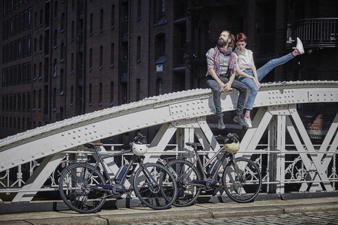 Germany, Hamburg, couple with electric bicycles sitting on railing of a bridge - RORF00649