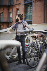 Deutschland, Hamburg, Hipster mit Elektrofahrrad steht auf einer Brücke in der Alten Speicherstadt - RORF00650