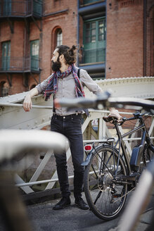 Germany, Hamburg, hipster with electric bicycle standing on a bridge at Old Warehouse District - RORF00650