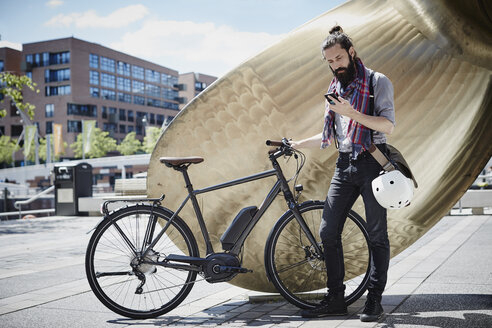 Man with electric bicycle looking at his cell phone - RORF00660