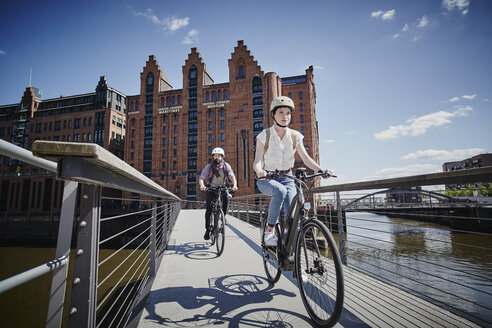 Germany, Hamburg, couple riding electric bicycles on bridge at Old Warehouse District - ROR00667