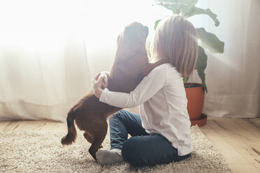 Kleines Mädchen sitzt auf dem Teppich und umarmt ihren Hund - RTBF00700