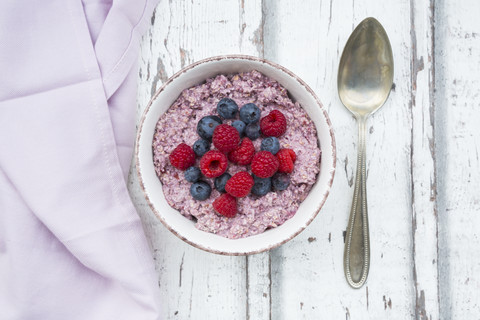 Schüssel mit Overnight Oats mit Blaubeeren und Himbeeren auf Holz, lizenzfreies Stockfoto