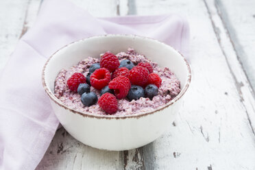 Schüssel mit Overnight Oats mit Blaubeeren und Himbeeren auf Holz - LVF05904