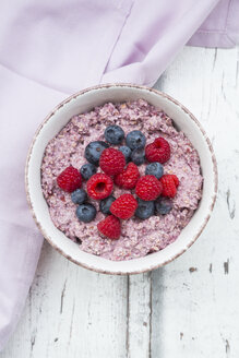 Schüssel mit Overnight Oats mit Blaubeeren und Himbeeren auf Holz - LVF05905