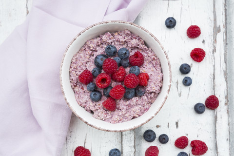 Schüssel mit Overnight Oats mit Blaubeeren und Himbeeren auf Holz, lizenzfreies Stockfoto