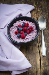 Schüssel mit Overnight Oats mit Blaubeeren und Himbeeren auf Holz - LVF05907