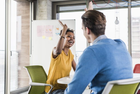 Happy young woman high fiving with colleague in office - UUF10011