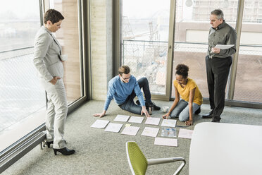 Businesspeople looking at documents on office floor - UUF10012