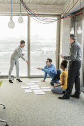 Businesspeople looking at documents on office floor - UUF10013