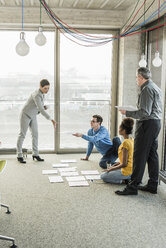 Geschäftsleute, die auf dem Boden eines Büros Dokumente betrachten - UUF10013