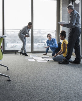 Businesspeople looking at documents on office floor - UUF10014