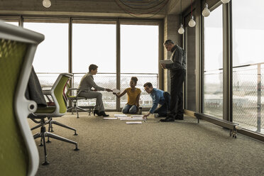 Businesspeople looking at documents on office floor - UUF10015